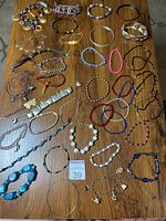 Overhead photo showing whole collection of more than 40 costume bracelets arranged on a wooden table with varied sizes, colors, and styles
