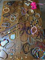 Overhead photo showing a diverse assortment of more than 60 costume jewelry bracelets spread on a wooden floor. Includes various styles such as bead bracelets, metal bangles, chain links, and fabric-strung.