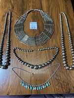 Five costume jewelry necklaces displayed on wooden surface including beaded and metallic designs, with a MaxSold auction tag visible.