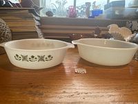 Photo of two white Fire-King casseroles with one showing green floral pattern and both with handles visible.