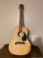 Full view of First Act acoustic guitar showing natural wood finish, black pickguard, and steel strings.