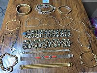 Photo showing 16 gold toned vintage costume bracelets arranged on a wooden surface, displaying variety of styles including thin bangles, mesh with enamel, large linked chains, and decorative wide bracelets.