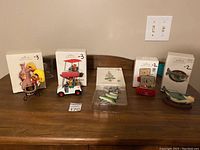 Five Hallmark Keepsake ornaments displayed on wooden table with original marked boxes behind them.