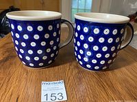Front view of two blue handmade Polish pottery mugs with white dot pattern and handles.