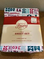 Full view of folded Destination Holiday twin sheet set with visible packaging and colorful holiday text pattern.