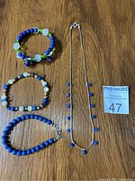 Photo showing the four jewelry pieces arranged on a wooden surface: a necklace and three bracelets, along with a MaxSold lot number card.