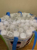 Top view of a reusable tote bag filled with numerous individually wrapped white foam light-up batons, showing bulb ends and plastic wrapping.