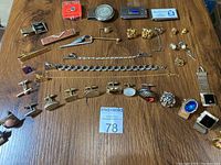 Full view of men's costume jewelry laid out including various money clips, tie bars, lapel pins, cuff links, chains, and buttons.