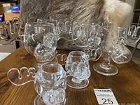 Set of four clear glass Bullwinkle moose head glasses and two small plastic shot glasses arranged on wood surface with fur background.