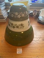 Front view showing set of three green and white Pyrex mixing bowls stacked, with floral patterns on top two bowls and solid green large bowl.