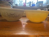 Two Pyrex mixing bowls side by side on a wooden surface, one beige with mushroom print, the other solid yellow.