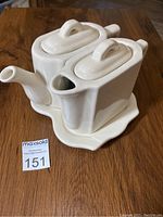 Photo showing three-piece white ceramic teapot, creamer, and tray set with lids in place, all with smooth glossy finish and modern rectangular design details.