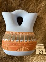 Photo showing frontal view of the Navajo wedding pottery vase highlighting the white matte finish, terracotta band with carved and painted traditional patterns, and the double spout with heart-shaped opening.
