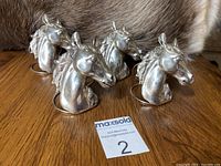Four signed pewter horse head napkin rings on wooden surface with fur background, showing all horse heads in profile and full set together.