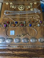 Six vintage belts laid out flat on wooden surface showing different metalwork styles and stones.