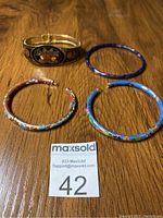 Four cloisonné bracelets shown from above, including two hinged bangles (one black with floral medallion, one turquoise with flowers), one larger hinged bracelet, and one solid blue bangle.