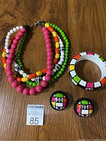 Top view of the multi-strand colorful beaded necklace, round bangle bracelet, and earrings on a wooden surface