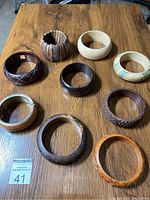 Nine wooden bracelets laid out on wooden table showing full variety of styles and colors.