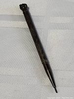 Antique sterling silver mechanical pencil displayed on a cloth background, showing ornate engraved design and a dark patinated finish.