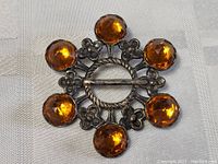 Front and back images of antique sterling silver brooch with six orange topaz-like stones and floral silver accents.