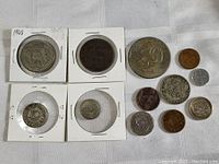 12 mixed coins shown on white fabric, some in white coin holders, varying sizes and colors, listing conditions from early 20th century to recent