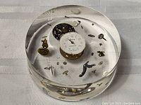 Circular clear resin paperweight showing embedded vintage watch parts including a Westclox watch face and various gears, springs, and dials.