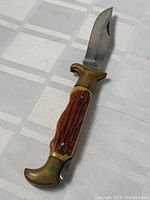 Full view of folding knife showing handle with brass guard and textured faux stag grips, blade partially opened.