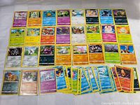 Photo showing an assortment of Pokemon cards laid out in a grid, displaying multiple character cards from the franchise with visible HP and attacks.