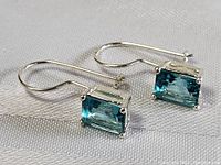 Pair of sterling silver aquamarine earrings on fabric background showing front view with light blue stones and hook style backs.