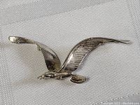 Close-up of sterling silver bird pendant in flight pose, showing wings spread wide and tail details.