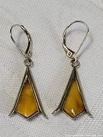 Pair of sterling silver dangle earrings featuring butter yellow amber stones with lever-back closures on white textured fabric background.