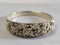 Close-up side view of sterling silver ring with raised lattice design and dark bead encrusting.