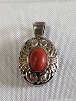 Front-facing view of the pendant showing the red coral stone side with detailed silver filigree work.