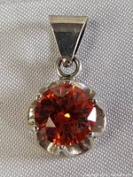 Close-up front view of the pendant showing the large round faceted orange-red gemstone set in a sterling silver scalloped claw setting.