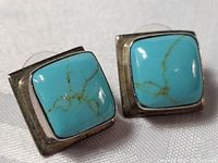 Close-up of the square turquoise stones with distinct veining and sterling silver setting on white fabric background.