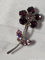Close-up image of the floral pin brooch showing the purple and pink crystals and silver-tone metal stem