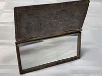 Inside open metal shaving mirror with clear reflective glass and metal frame.