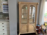 Full frontal view of the wood display cabinet showcasing glass front doors and carved lower panels.