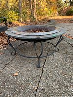 Fire pit shown from side angle, highlighting the curved wrought iron legs and marble surround on stand.