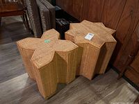 Two woven rattan side tables/stools in Mid-Century Modern style, star-shaped, placed on floor near wood-paneled wall.