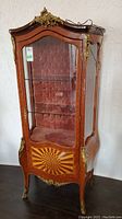 Front view of wood curio cabinet with glass door and padded back