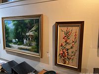 Two framed paintings hung on a white wall, the larger landscape painting on the left and smaller floral painting on the right.