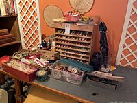Overall photo of a table with a wooden thread display rack holding multiple spools of thread, various containers with craft notions, ribbons, and trims.