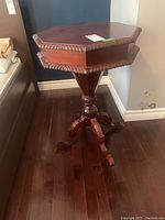 Front view of octagonal wooden sewing side table with detailed carved edges and pedestal base