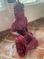 Front-side view of seated red painted Buddhist statue showing hand resting on knee and detailed headdress.