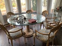 Full view of round glass top table surrounded by six matching chairs in front of windows