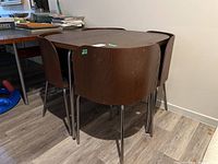 Square wood top table with metal hairpin legs. Four chairs tuck neatly into corners underneath the table, showing compact design.