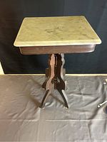 Front view of the vintage accent table showing square marble top and wooden carved base with three legs.