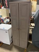 Closed front view of a tall gray plastic storage cabinet with two paneled doors and handles in a garage environment.
