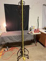 Full view of the ornate metal coat rack with a measuring tape extended alongside showing approximately 68 inches in height.